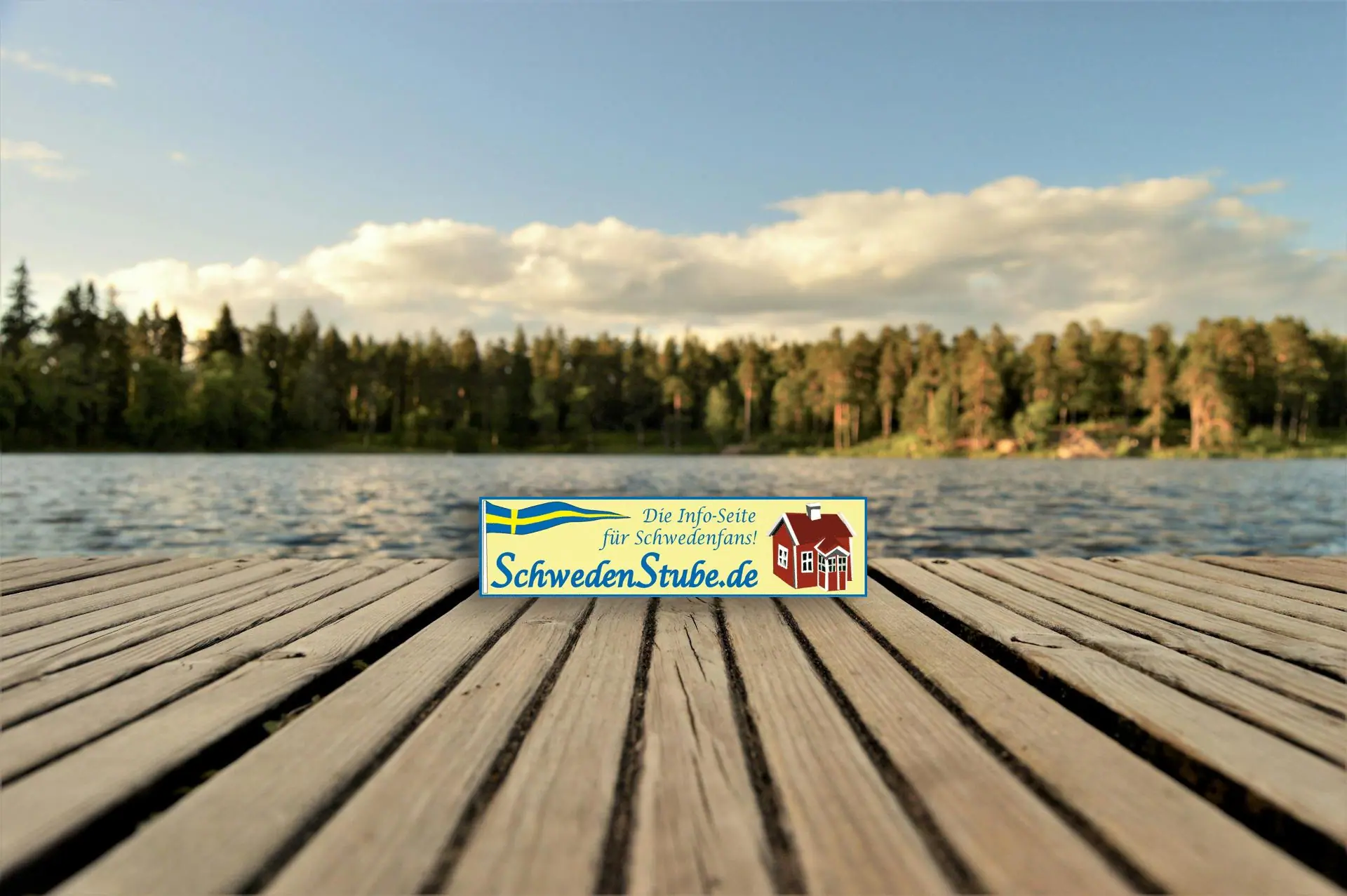 See mit strahlend blauem Himmel mit Bootssteg in Schweden, darauf das Logo der Schwedenstube